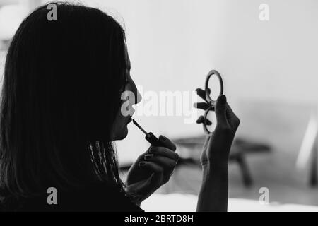 Jeune et belle femme cherche à miroir et à peindre ses lèvres. Maquillage et concept cosmétique Banque D'Images