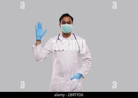 Docteur agitant la main portant un masque médical et des gants isolés. Indian Man Doctor dire Bonjour, geste de bienvenue. Medic Banque D'Images