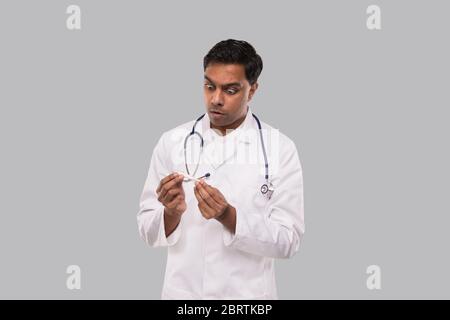 Thermomètre à observation médicale Shokk Sminder isolé. Indian Man Doctor souriant avec thermomètre en mains. Vie saine, Docteur, concept de virus. Medic Banque D'Images