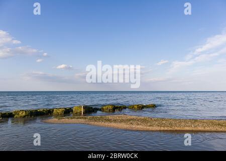 Une petite bande de sable menant à un brise-lames naturel. Avec un ciel bleu et clair et des nuages sur l'arrière-plan. Banque D'Images