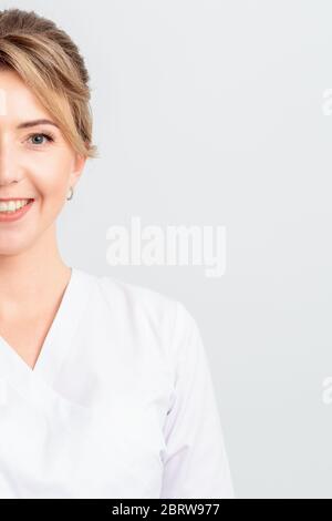 Portrait à moitié de visage de beau médecin ou stagiaire ou cosmetologiste en robe blanche se tient souriant à l'appareil photo, isolé sur fond blanc. Banque D'Images