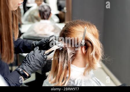 Coiffeur mains teindre cheveux de jeune femme dans salon de coiffure. Banque D'Images