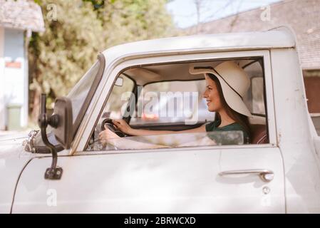 Une belle jeune femme avec un chapeau de paille conduit un vieux camion blanc. La vie dans un village Banque D'Images