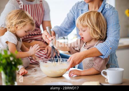 Section moyenne de la jeune famille avec deux petits enfants à l'intérieur dans la cuisine, la cuisine. Banque D'Images