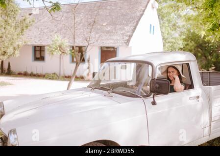 Une belle jeune femme avec un chapeau de paille conduit un vieux camion blanc. La vie dans un village Banque D'Images