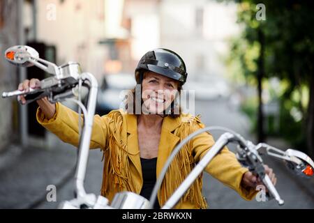 Femme âgée et gaie voyageant en ville avec une moto. Banque D'Images