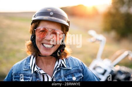 Une femme âgée et gaie voyageant à moto à la campagne au coucher du soleil. Banque D'Images