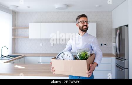 Homme mature debout dans une maison non meublée, tenant une boîte mobile. Banque D'Images