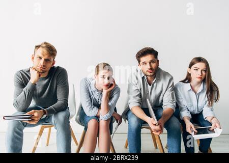 Groupe de jeunes candidats avec CV et gadgets regardant l'appareil photo dans le bureau Banque D'Images