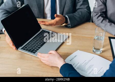 Vue rognée du recruteur pointant sur l'ordinateur portable avec écran vide près de la femme avec CV pendant l'entrevue d'emploi Banque D'Images