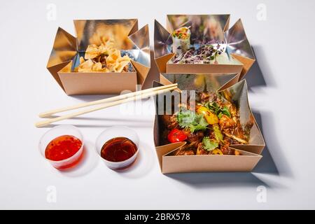sauces épicées et baguettes à proximité des boîtes à emporter avec des plats chinois préparés sur du blanc Banque D'Images