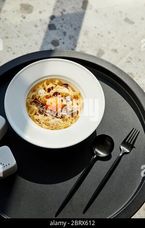délicieux pâtes carbonara servi avec des couverts sur table noire sur fond de marbre au soleil Banque D'Images