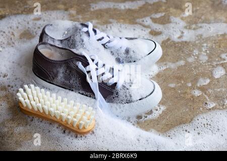 Baskets avec mousse de détergent en poudre, eau de dissolution et brosse en bois sur sol en ciment. Lavage des chaussures sales. Banque D'Images