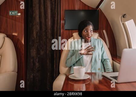 choqué femme d'affaires afro-américaine dans un avion privé touchant la poitrine tout en regardant dans le hublot Banque D'Images