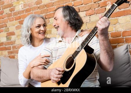 homme heureux et mature jouant de la guitare acoustique près de la femme gaie Banque D'Images