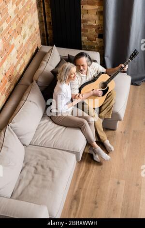 vue aérienne sur un homme barbu et mature jouant de la guitare acoustique près d'une femme joyeuse Banque D'Images