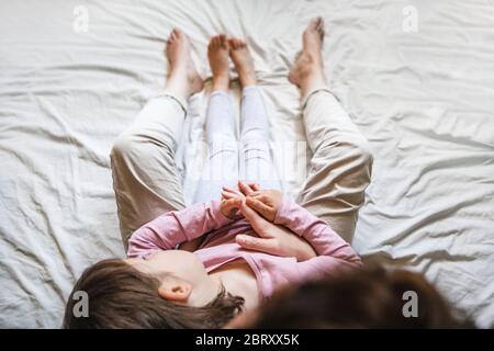 Une petite fille se repose sur la poitrine de sa mère dans le lit comme ils tiennent les mains ensemble. Maman l'enveloppe dans ses bras comme un signe d'amour Banque D'Images