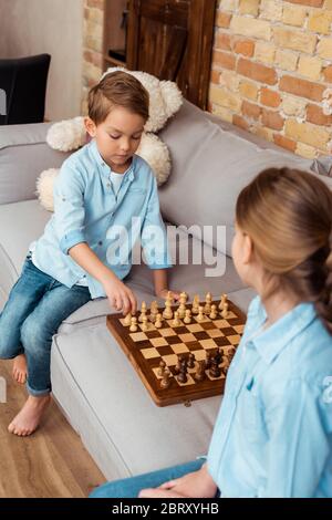 attention sélective aux frères et sœurs jouant aux échecs sur le canapé dans le salon Banque D'Images