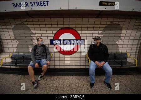 Deux hommes dans les masques faciaux sont assis devant l'œuvre d'art de Sherlock Holmes dans la station de métro Baker Street à Londres le jour de Sherlock Holmes, après l'introduction de mesures pour sortir le pays du confinement. Banque D'Images