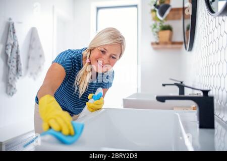 Femme âgée avec des gants nettoyant la salle de bains à l'intérieur à la maison. Banque D'Images