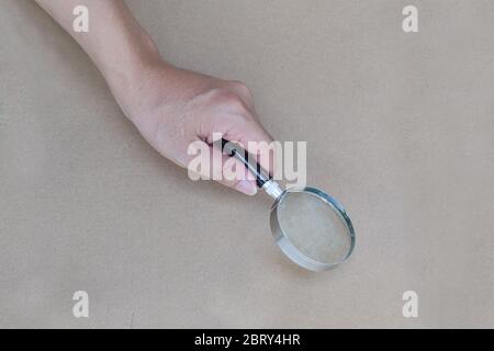Main tenant une loupe avec fond de papier marron. Banque D'Images