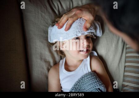 Un père méconnaissable s'est posé sur un petit fils malade allongé dans un lit à l'intérieur de la maison. Banque D'Images