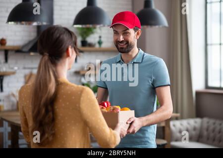 Une cliente aux cheveux foncés reçoit des produits d'épicerie du coursier dans la cuisine Banque D'Images