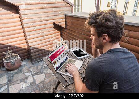 KIEV, UKRAINE - 13 AVRIL 2019: Jeune homme utilisant un ordinateur portable avec le site d'Ebay tout en étant assis sur un balcon Banque D'Images