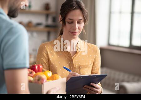 Une cliente à poil sombre signe le bordereau de marchandises après avoir reçu les produits d'épicerie Banque D'Images