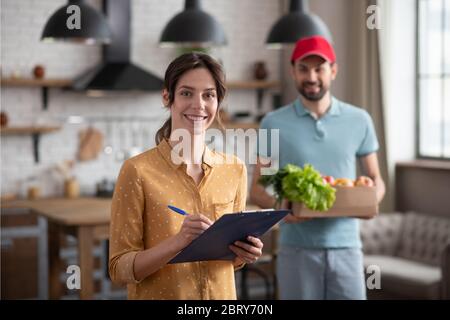 Une cliente aux cheveux sombres souriant tout en recevant les produits du coursier Banque D'Images