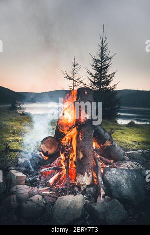 Petit feu de camp avec de légères flammes au bord d'un lac pendant un coucher de soleil lumineux. Belis, Cluj, Roumanie Banque D'Images