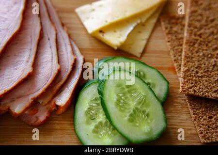 Trancher du jambon, des concombres et du fromage avec des pains fins et grossiers se trouvent sur une planche en bois. Banque D'Images