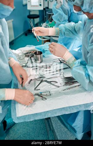 Instruments stériles sur la table d'opération, une équipe de médecins présente les instruments pour l'opération. De nombreuses mains sont en train de préparer des gants stériles. Banque D'Images