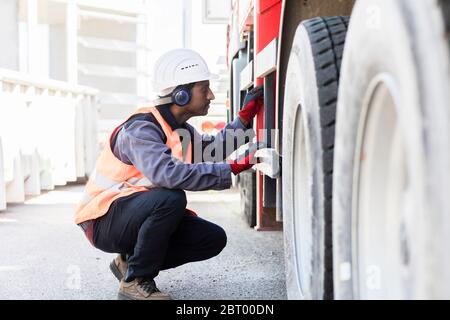 Un ingénieur de maintenance portant un casque et des protections auditives vérifie le train de roulement d'un camion. Banque D'Images