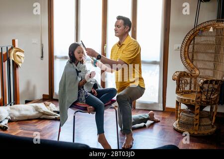 Le père coupe les cheveux de sa fille à la maison, pendant le séjour à la période de verrouillage à la maison. Banque D'Images