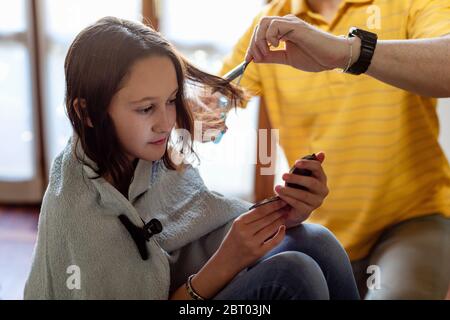 Le père coupe les cheveux de sa fille à la maison, pendant le séjour à la période de verrouillage à la maison. Banque D'Images