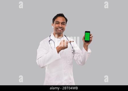 Médecin pointant sur Phone Isolated. Indian Man Doctor Phone écran vert entre les mains. Medic Banque D'Images
