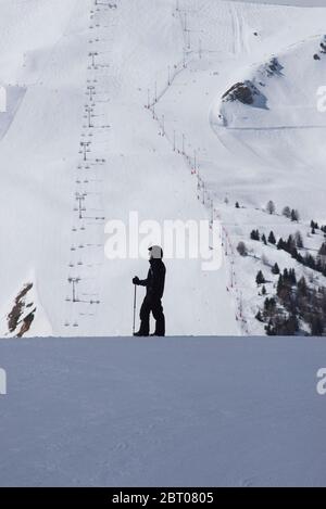 Femme skieuse debout en profil avec une piste de ski éloignée à la Plagne, Savoie France Banque D'Images