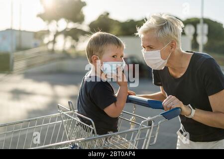 Mère jouant avec joie avec un enfant assis dans un chariot. Les deux portent un masque de protection avant d'entrer dans un supermarché. Banque D'Images