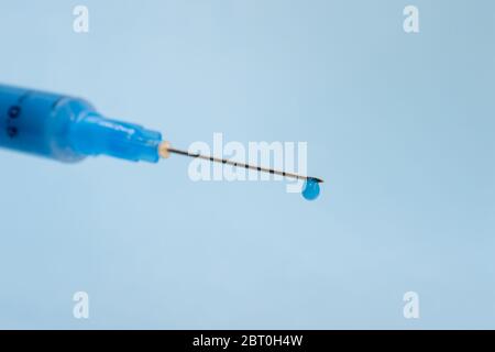 Gros plan d'une aiguille de seringue avec une goutte de solution à l'extrémité sur fond bleu. Banque D'Images