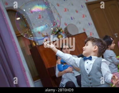 Joli petit garçon attrapant des bulles de savon . Petit garçon blond jouant avec des bulles de savon . Enfants à la fête. Des bulles de savon apparaissent. Fête d'enfants. À Banque D'Images