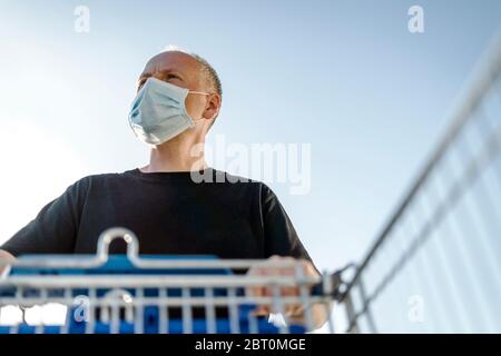 Homme portant un masque facial de protection poussant chariot prêt pour faire du shopping dans le supermarché Banque D'Images