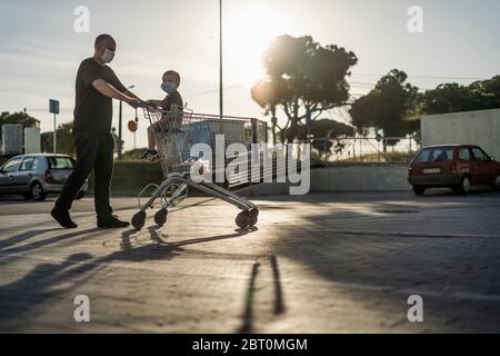 Père poussant le chariot avec son petit fils sur un parking. Les deux portent des masques de protection. Banque D'Images