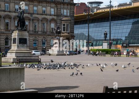 George Square, comme les gens de distance sociale sur les bancs d'une chaude journée ensoleillée avec la station de Queen Street récemment rénovée visible dans l'arrière-plan. Banque D'Images