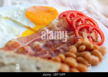 Gros plan sur le petit déjeuner anglais traditionnel : œufs frits, bacon, haricots, pain grillé et tomates sur une assiette. Banque D'Images