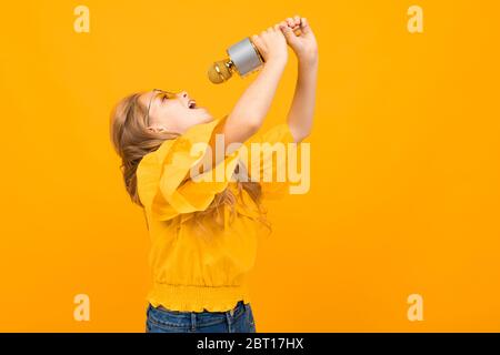 Portrait de la jeune fille caucaienne avec de longs cheveux équitables dans des verres jaunes sourires et chante des chansons avec un microphone Banque D'Images