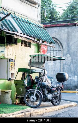 Un pédicab traditionnel ou un pousse-pousse est stationné à côté d'une moto moderne dans les rues de la vieille ville fortifiée d'Intramuros Manille, aux Philippines. Banque D'Images