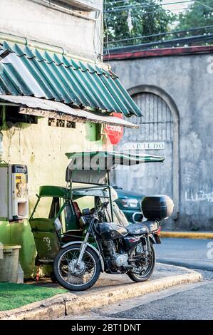 Un pédicab traditionnel ou un pousse-pousse est stationné à côté d'une moto moderne dans les rues de la vieille ville fortifiée d'Intramuros Manille, aux Philippines. Banque D'Images