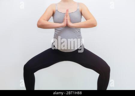 Femme enceinte non reconnaissable pratiquant le yoga dans la pose de cheval sur fond blanc avec espace de copie Banque D'Images