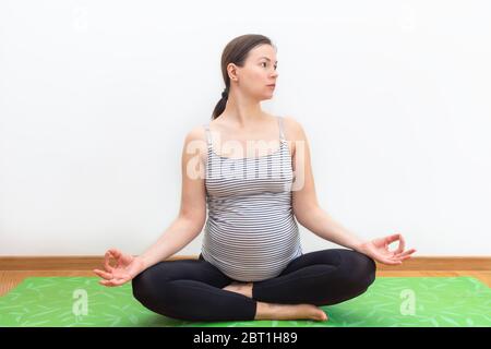 Femme enceinte assise en position lotus et pratiquant le yoga à la maison. Maternité, grossesse, concept de yoga Banque D'Images